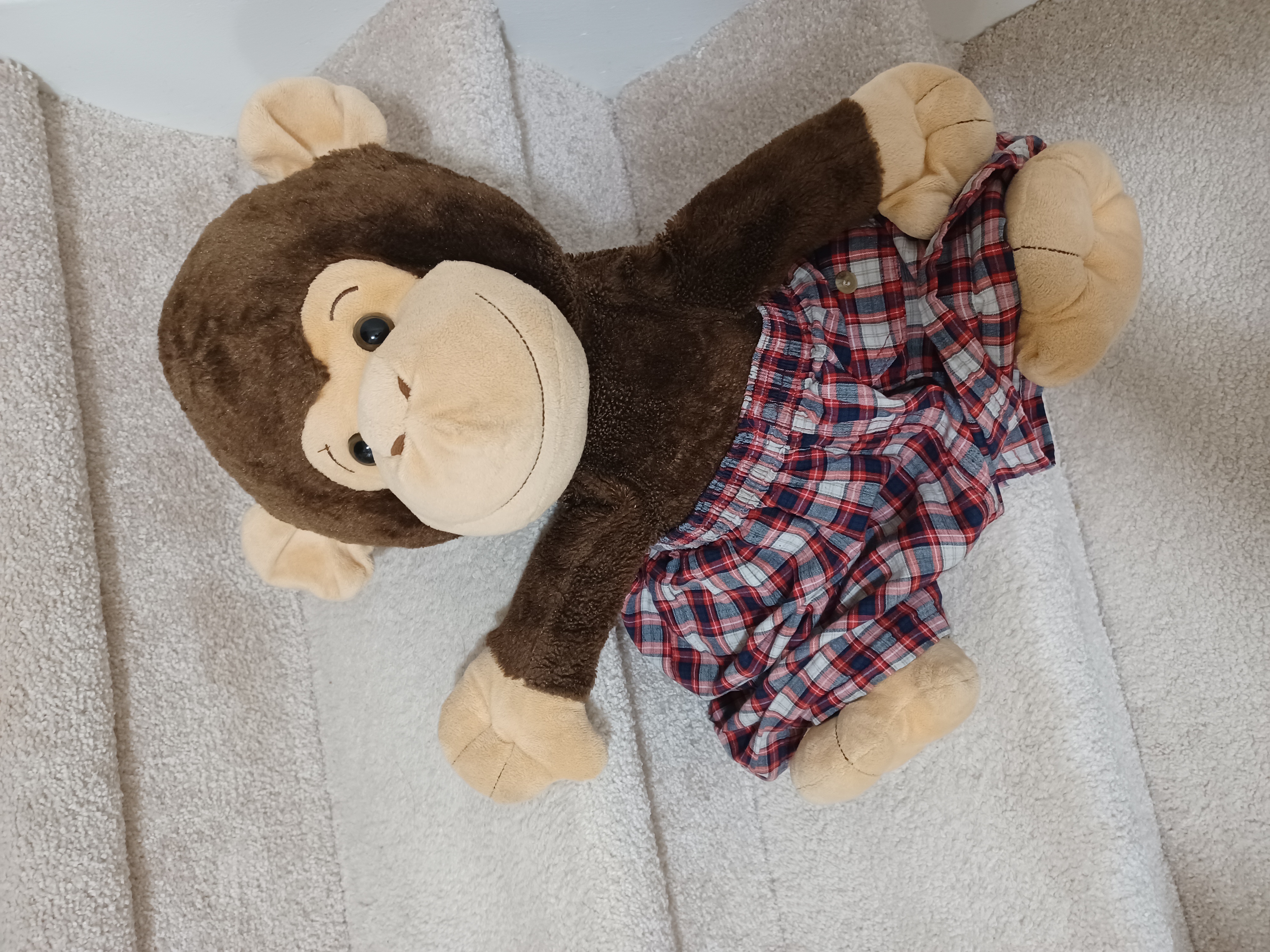 stuffed monkey wearing plaid shorts while sitting on staircase